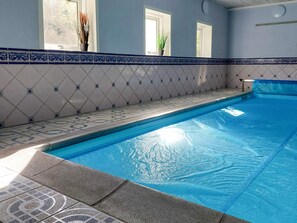 Ein Schwimmbecken mit einer gefliesten Kante, eine Wand mit Diamantmusterfliesen und ein Fenster mit einer Pflanze.