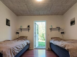 Ein Zimmer mit zwei Betten, einer zur Außenseite führenden Tür und Regalen an der Wand mit diversen Gegenständen.