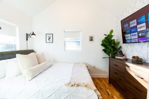 A bedroom with a bed, a dresser, a TV mounted on the wall, and a window.