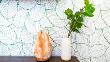 A rock salt formation and a potted plant on a wooden surface against a leaf-patterned wall.