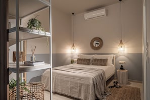 A bedroom with a bed, bedside tables, a wall-mounted air conditioner, and a hanging light fixture. - Ninemia Shore Retreat | Beachfront Escape with Hot Tub (Stalida)