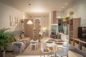 A modern living room with a sofa, dining table, and chairs, a kitchen area with a microwave and toaster, and a TV. - Ninemia Shore Retreat | Beachfront Escape with Hot Tub (Stalida)