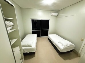 Ein kleines Zimmer mit zwei Einzelbetten, einem Kleiderschrank, einer Schiebetür und einer Klimaanlage.