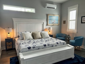 Une chambre à coucher avec un lit, deux tables de chevet, une chaise, une fenêtre avec des stores et un tableau au mur.