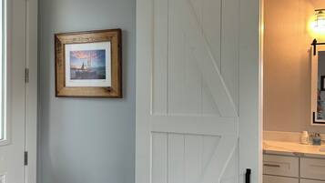 A room with a white sliding barn door, a framed picture on the wall, and a bathroom with a sink and mirror.