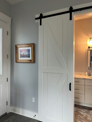 Une pièce avec une porte coulissante blanche de style grange, un tableau encadré au mur et une salle de bain équipée d’un lavabo et d’un miroir.