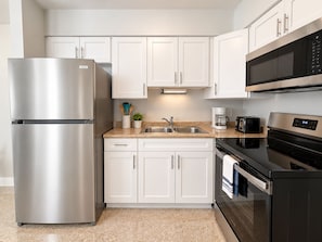 A modern kitchen with stainless steel appliances, white cabinetry, and a granite countertop. - 1BR Beachfront Cottage, Dogs Welcome, Steps to the Sand (Redington Shores)