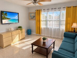 A living room with a television, sofa, coffee table, and a ceiling fan. - 1BR Beachfront Cottage, Dogs Welcome, Steps to the Sand (Redington Shores)