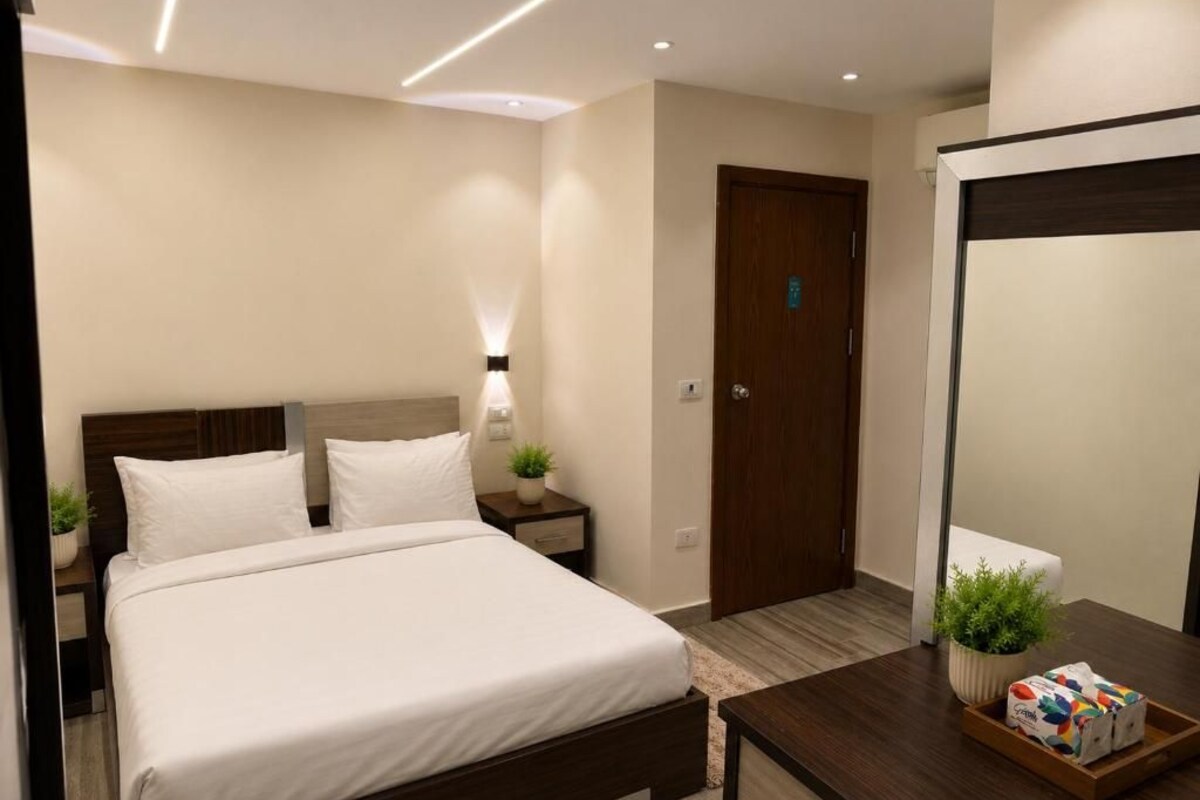 Una habitación de hotel moderna con cama, mesita de noche, lámpara y espejo.