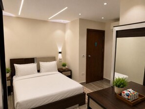 Una habitación de hotel moderna con cama, mesita de noche, lámpara y espejo.