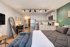 Camera d'albergo compatta con un letto, un divano, una scrivania, un angolo cottura e una televisione.