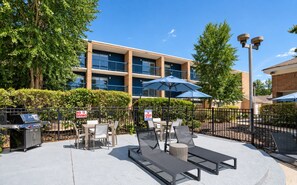 Ein Außenbereich mit Terrasse, Tischen, Stühlen, einem Grill und Sonnenschirmen.