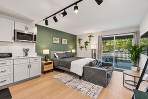 Ein modernes Schlafzimmer mit Bett, Nachttischen, einer Sitzecke, einem Balkon mit Aussicht und einer Küchenzeile.