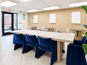 Una sala conferenze con un lungo tavolo, sedie blu e tavolini rotondi.