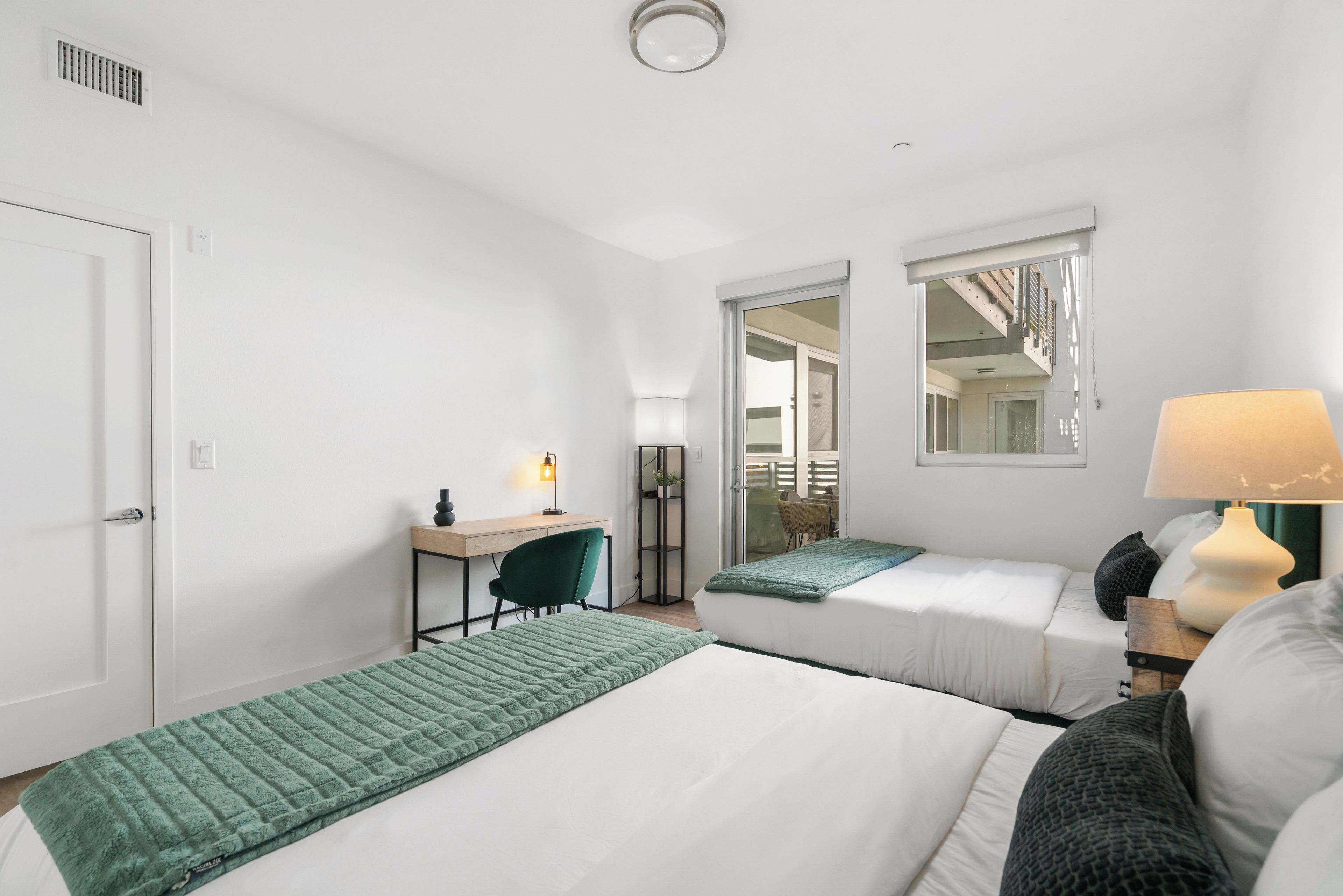 A hotel room with two beds, a desk, a chair, and a lamp.