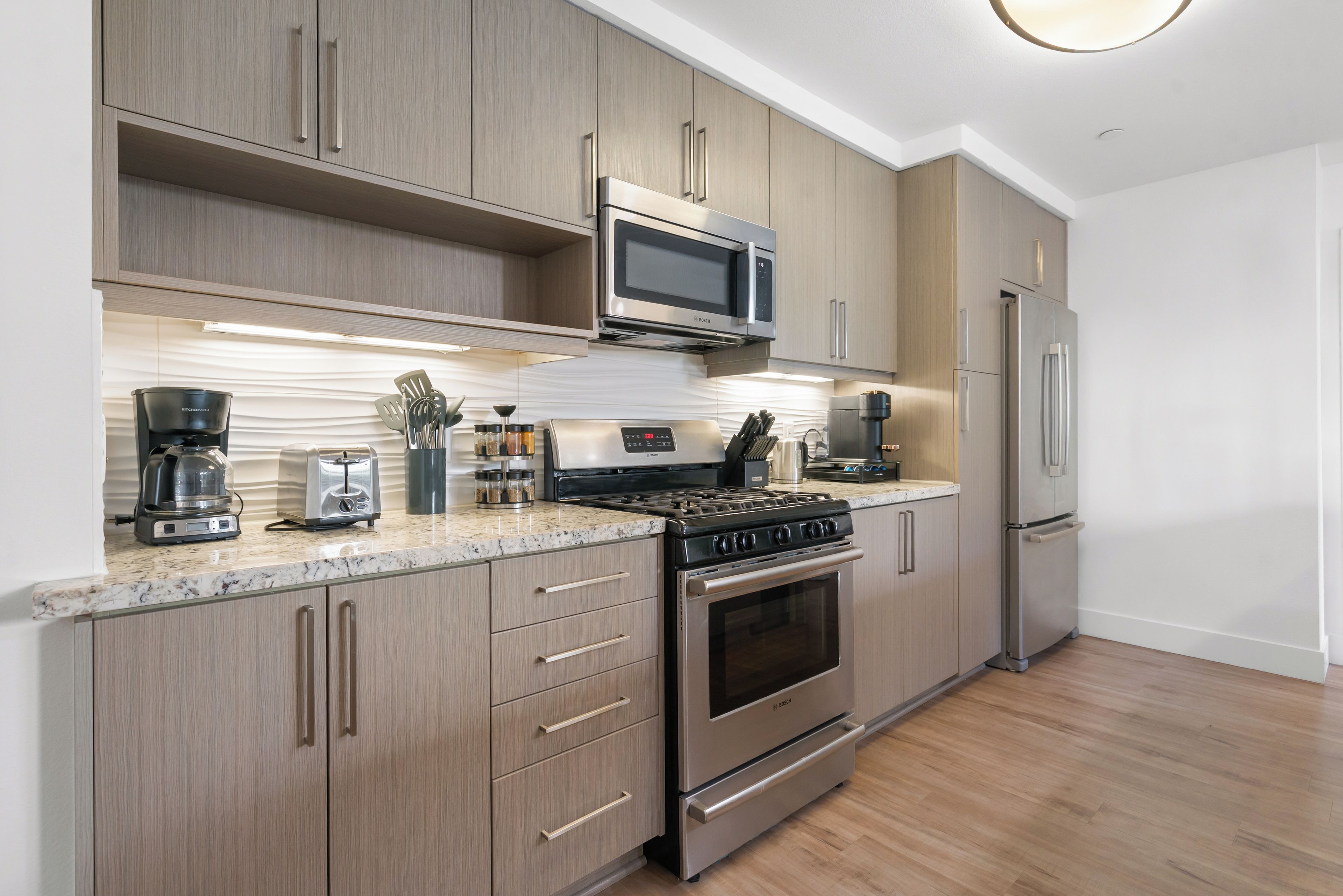 A modern kitchen with stainless steel appliances, wooden cabinets, and a marble countertop.