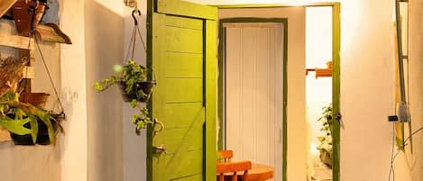 A small, enclosed space with a green door, a wooden table, and chairs, and a blue mat at the entrance.