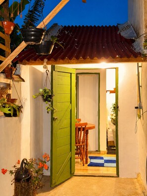 Ein kleiner, abgeschlossener Raum mit einer grünen Tür, einem Holztisch, Stühlen und einer blauen Matte am Eingang.