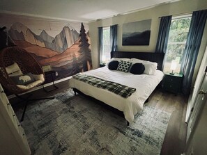 A bedroom with a large bed, a wall mural, a chair, and a window with curtains. - Cozy 2 Bedroom Retreat in the Heart of Cary, Near SAS (Cary)