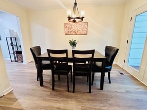 A dining area with a table and four chairs, a chandelier, a framed picture on the wall, and a potted plant. - Cozy 2 Bedroom Retreat in the Heart of Cary, Near SAS (Cary)