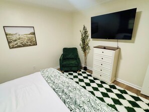 A bedroom with a bed, a dresser, a chair, a television, and a wall-mounted picture. - Cozy 2 Bedroom Retreat in the Heart of Cary, Near SAS (Cary)