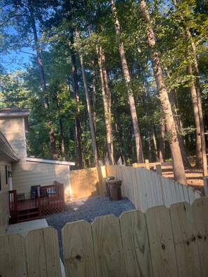 A wooden deck with a small table and chairs, surrounded by a wooden fence, and a building with a window to the left. - Cozy 2 Bedroom Retreat in the Heart of Cary, Near SAS (Cary)