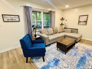 A living room with a blue armchair, a beige sectional sofa, a coffee table, and a patterned rug. - Cozy 2 Bedroom Retreat in the Heart of Cary, Near SAS (Cary)