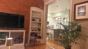 A living room with a TV, shelves with various items, a plant, and a view into the kitchen. - Stunning Victorian home with easy access to the best of Boulder - and Sundance! (Boulder)