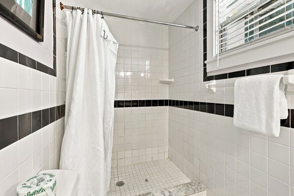 A bathroom with white tiles, a shower curtain, a towel rack, and a toilet.