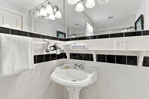 Une salle de bain avec un lavabo blanc, des murs carrelés en noir et blanc, un porte-serviettes et un miroir.