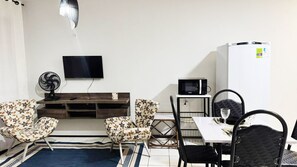 Un espace de vie compact comprenant un téléviseur à écran plat, un four à micro-ondes, un réfrigérateur et un coin repas avec deux chaises et une table.