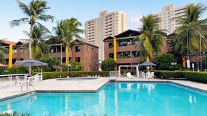 A swimming pool with a clear blue water, surrounded by palm trees and a building with multiple floors. - Comfort on Praia do Futuro by Reserva Mar (Fortaleza)