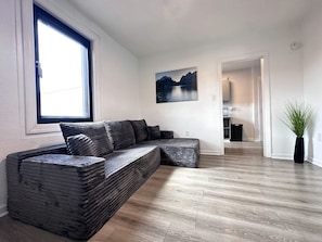 Ein modernes Wohnzimmer mit einer Eckcouch, einem großen Fenster und Blick auf einen Bergsee.