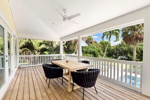 A covered outdoor area with a wooden deck, a table with chairs, and a white railing. - Coastal Retreat - Sanibel Island Home, Pool and Beach Access! (Sanibel)