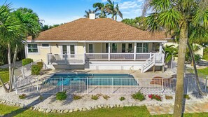 Ein zweistöckiges Haus mit Swimmingpool, überdachter Terrasse und umzäunter Veranda.
