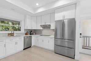 A modern kitchen with white cabinetry, a stainless steel refrigerator, and a window with a view of greenery. - Coastal Retreat - Sanibel Island Home, Pool and Beach Access! (Sanibel)