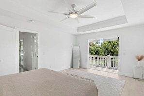 Une chambre avec un lit, un ventilateur de plafond, une grande fenêtre et une vue sur la verdure.