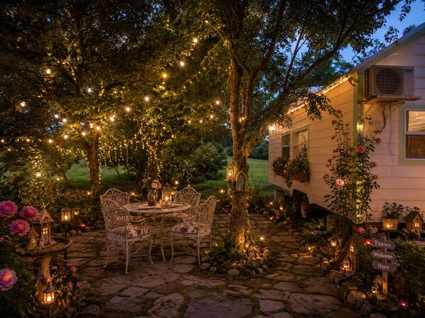 A rustic outdoor setting with a stone pathway, white metal chairs, and string lights.