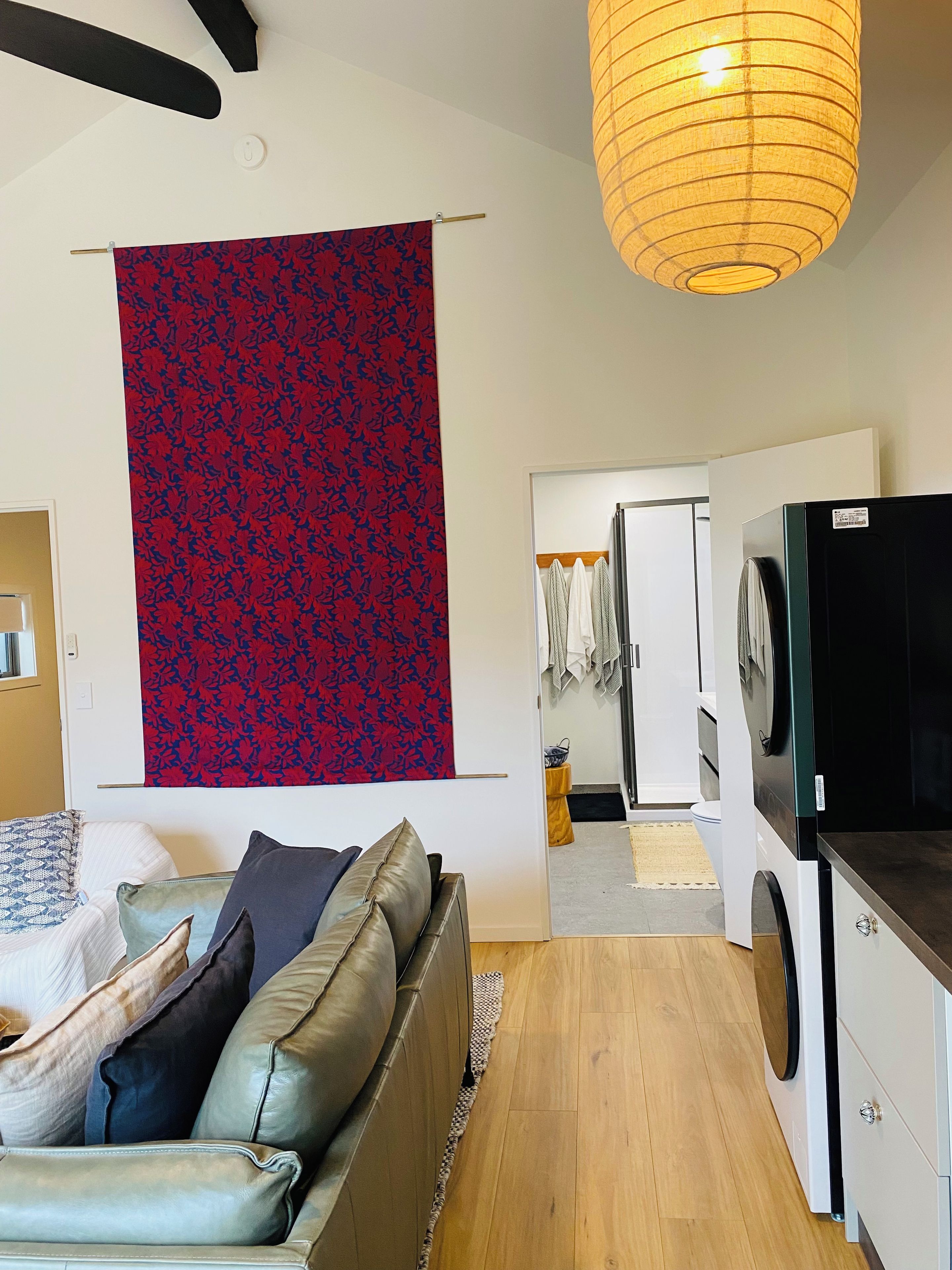 A modern living room with a sofa, a hanging tapestry, a washing machine, and a laundry area.