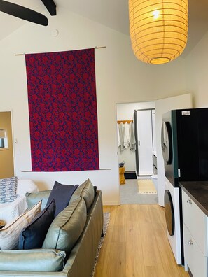 A modern living room with a sofa, a hanging tapestry, a washing machine, and a laundry area. - Lady Gs Guesthouse | Gorgeous escape for 2 (Geraldine)