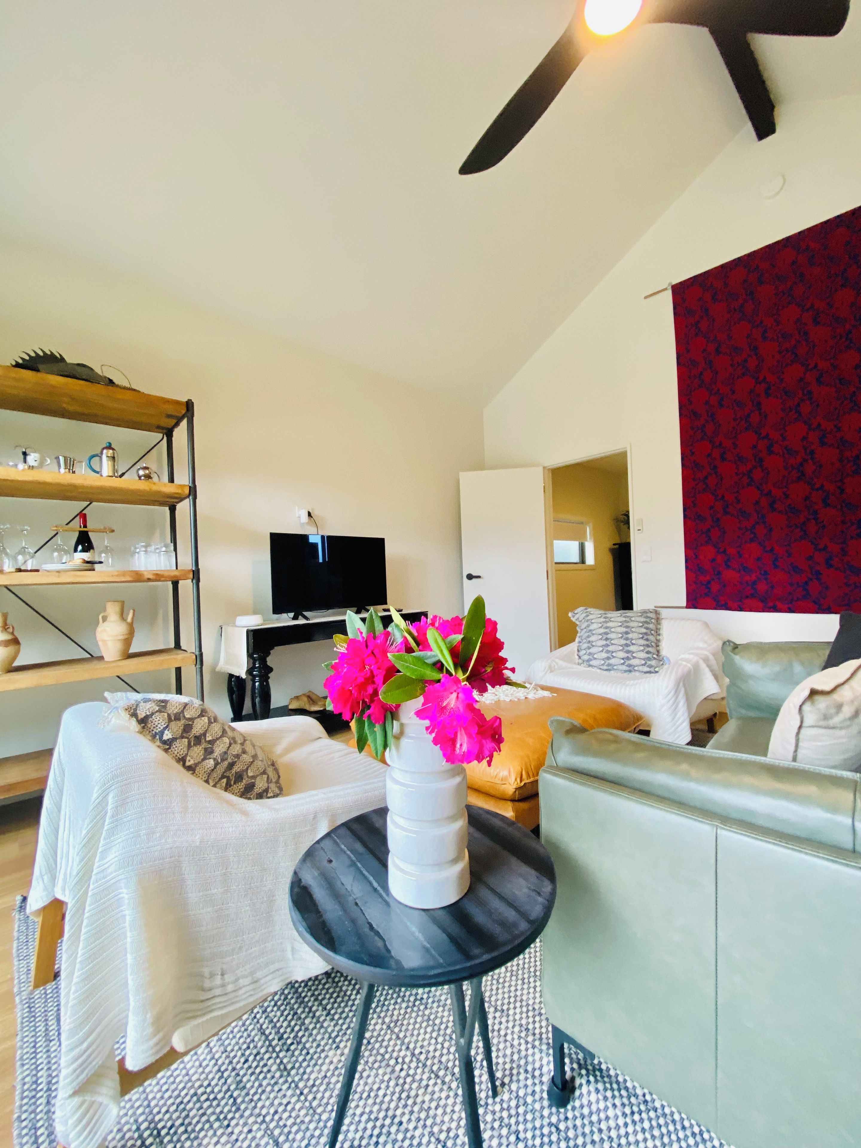 A modern living room with a sofa, a small round table with a vase of flowers, a television, and a bookshelf.