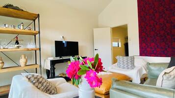 A modern living room with a sofa, a small round table with a vase of flowers, a television, and a bookshelf.