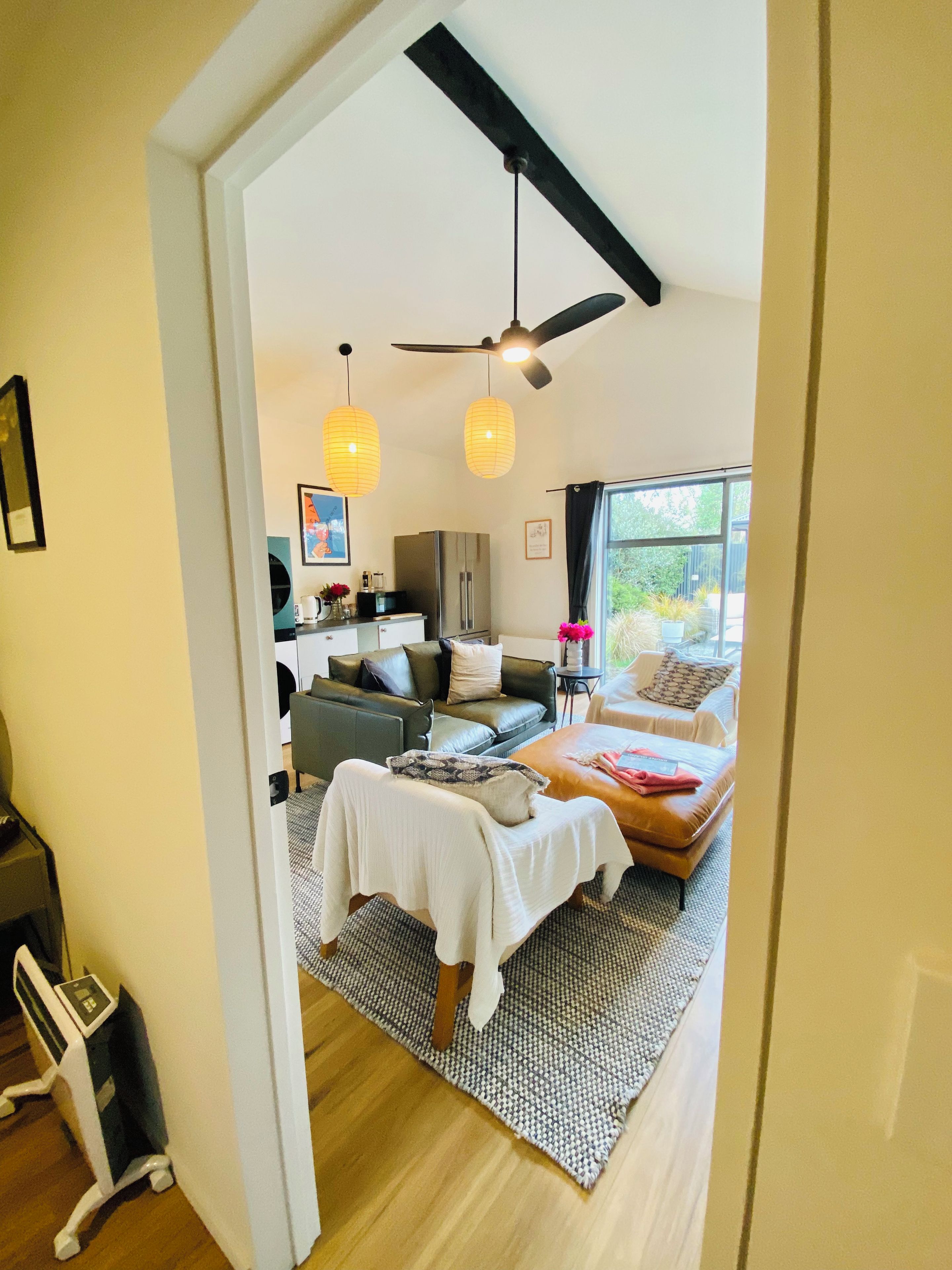 Un intérieur moderne comprenant un lit, un canapé et un coin repas, agrémenté d’un ventilateur de plafond, de luminaires suspendus et offrant une vue sur l’extérieur.
