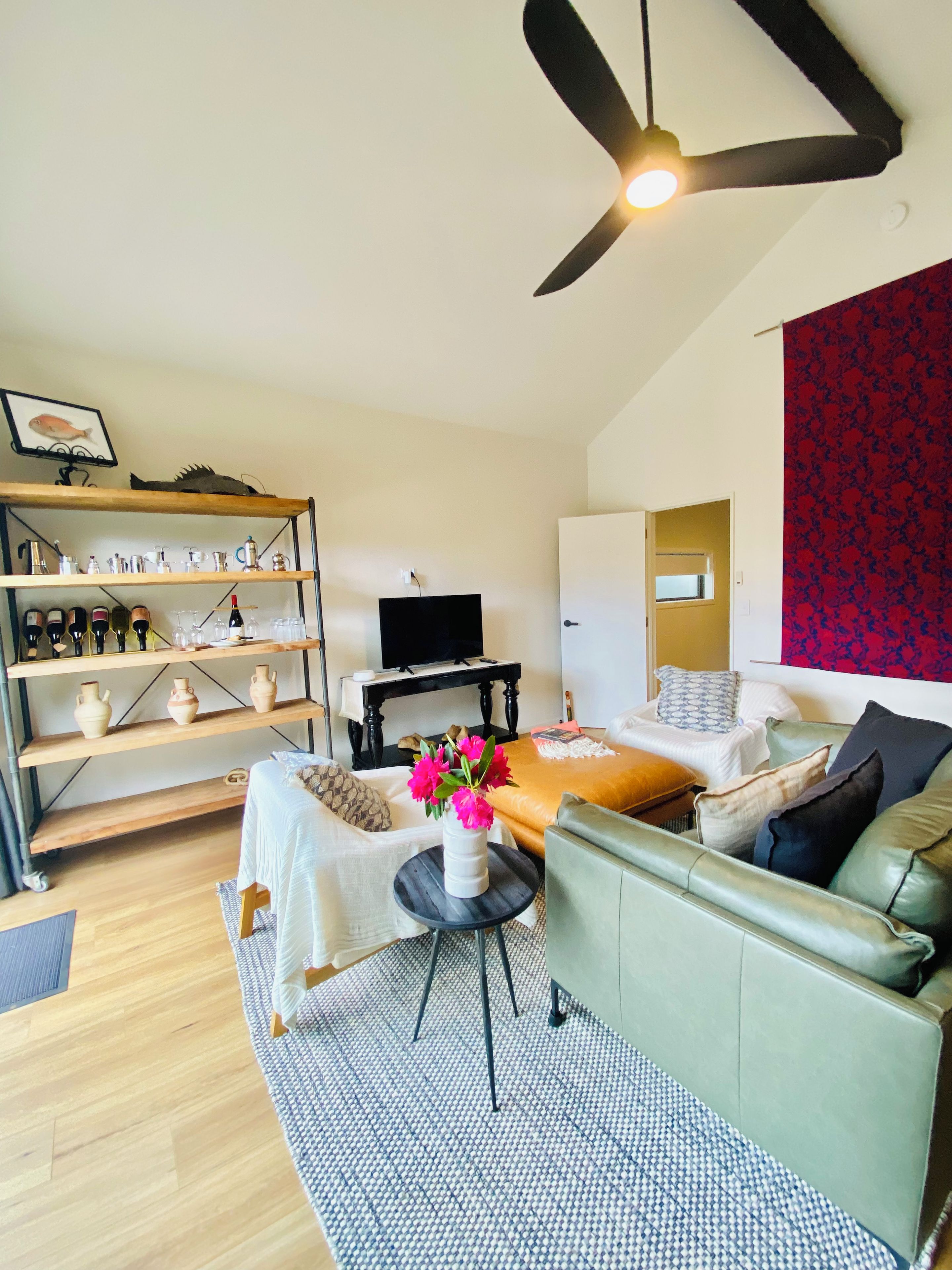 A modern living room with a sofa, a coffee table, and a TV. There is a bookshelf with various items and a ceiling fan.