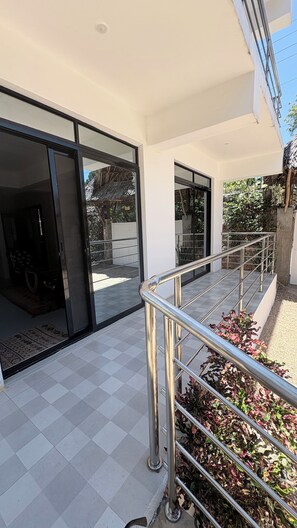 Entrada de um edifício com porta de vidro, guarda-corpo de metal e chão de azulejos.