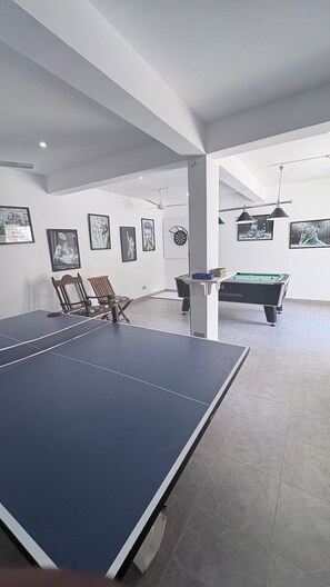 Ein geräumiger Raum mit Tischtennisplatte, Billardtisch und verschiedenen gerahmten Kunstwerken an den Wänden.
