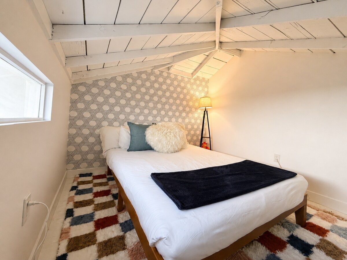 A bedroom with a bed, patterned wallpaper, a lamp, and a rug.