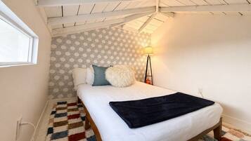 A bedroom with a bed, patterned wallpaper, a lamp, and a rug.