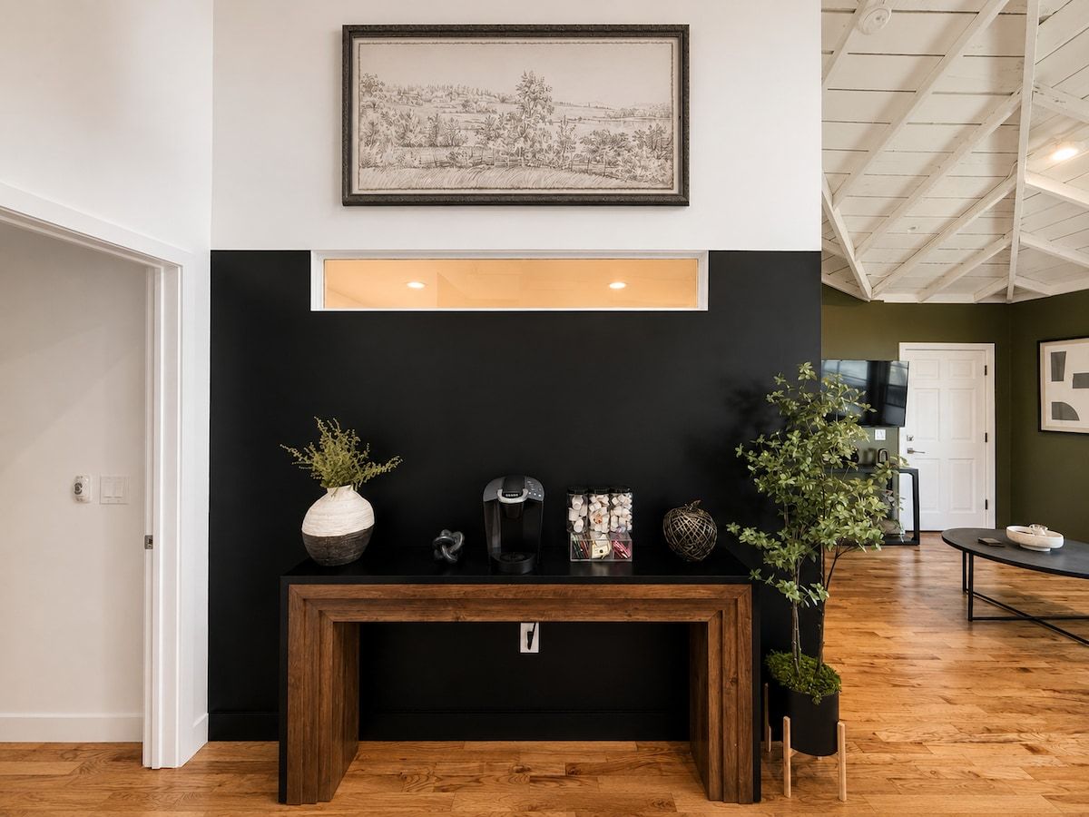 A modern interior with a black console table, a framed landscape painting, and a potted plant.