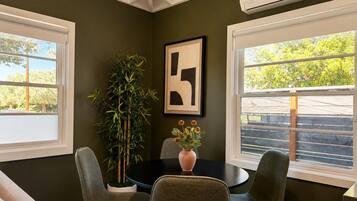 A room with a dining table, four chairs, a potted plant, and a framed artwork on the wall.